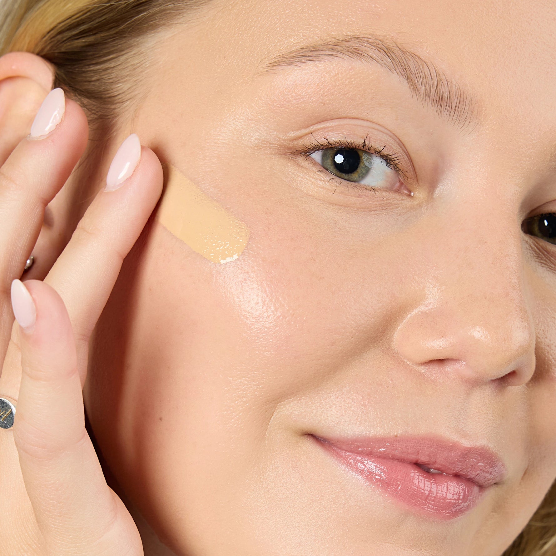 Close-up of a woman applying a beige concealer stick to her face Shade MN3 
