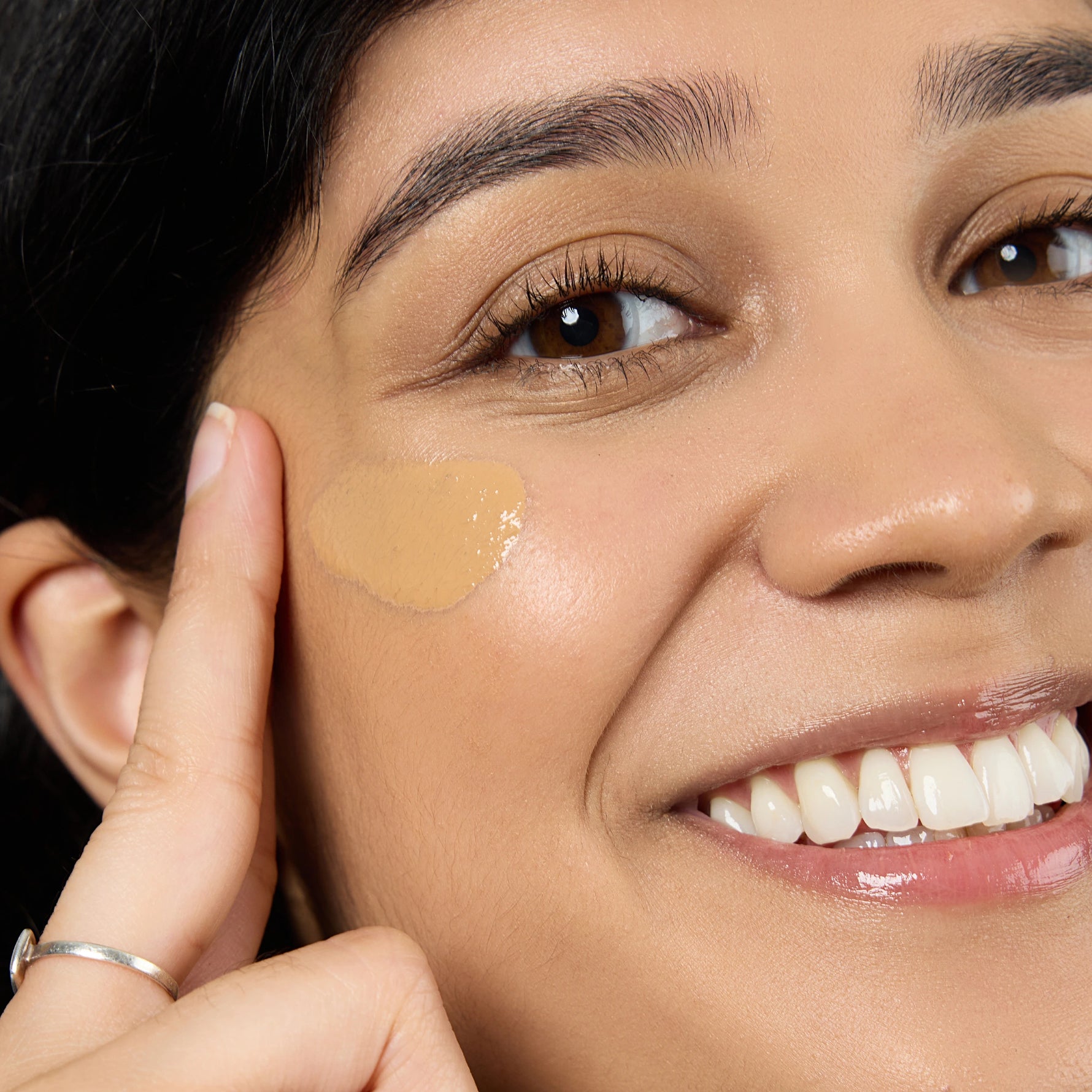 Close-up of a woman applying a beige concealer stick to her face Shade TN2 